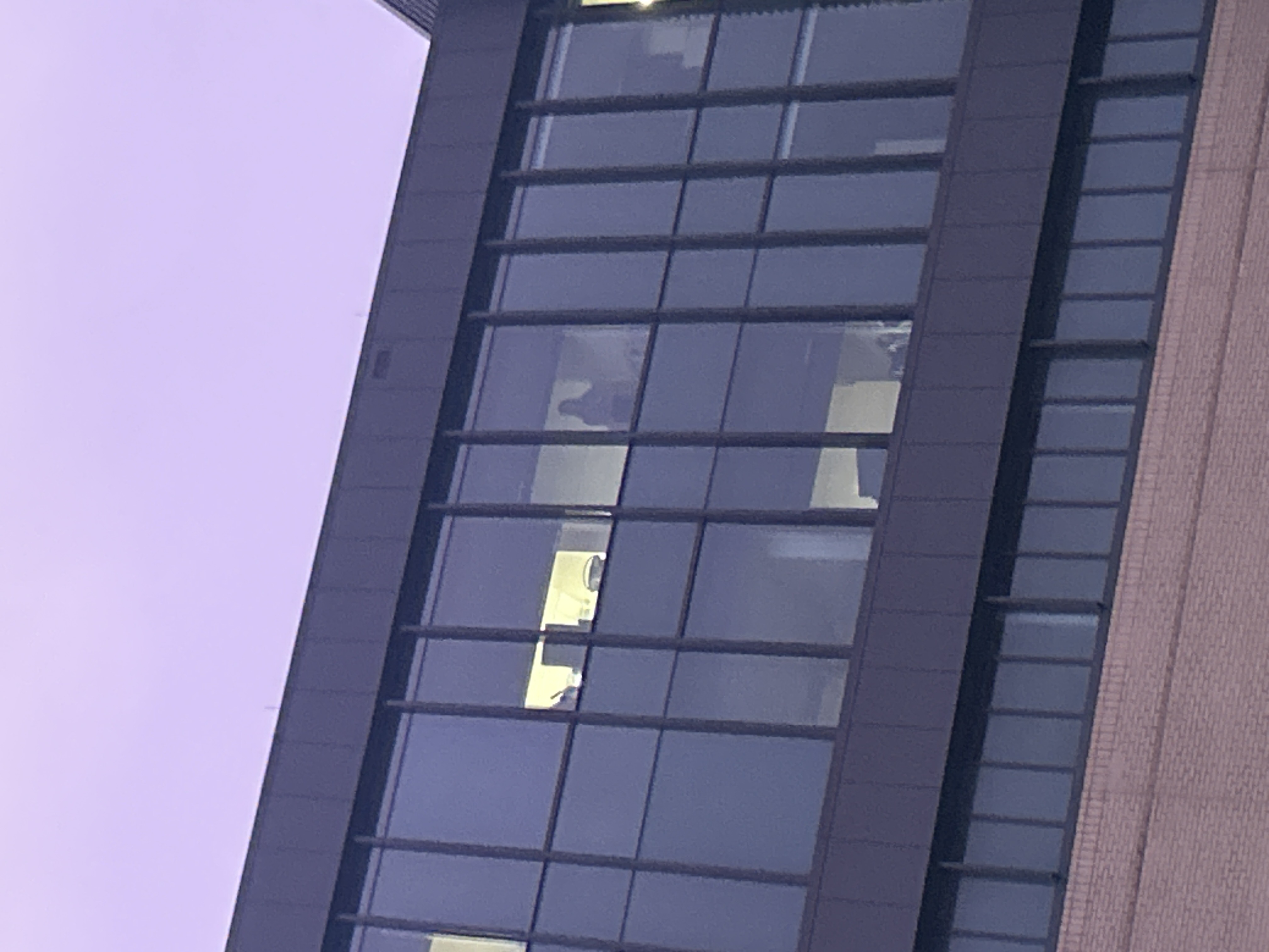 Image of a tall building with windows. The shadow of a person is standing at the window looking down at the person taking the photo.